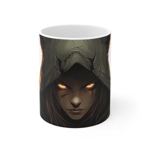 May include: A white ceramic mug featuring a graphic of a woman with dark hair and a hooded cloak. Her eyes are glowing orange.