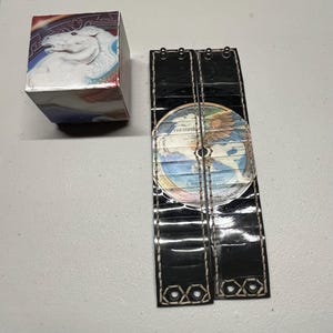 May include: Two black leather bracelets with white stitching. Each bracelet features a circular cutout with a vinyl record inside. The record is a copy of "The Steve Miller Band - The Joker".