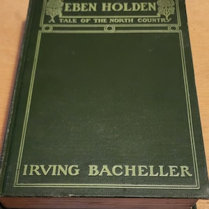 Puede incluir: Un libro antiguo de tapa dura titulado "EBEN HOLDEN A TALE OF THE NORTH COUNTRY" de Irving Bacheller. La cubierta es de color verde oscuro con letras doradas y elementos decorativos. El lomo del libro es visible, mostrando el papel envejecido.