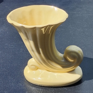 Może przedstawiać: Żółty ceramiczny wazon w kształcie rogu z żebrowanym wzorem. Wazon ma szeroki otwór i zaokrągloną podstawę.