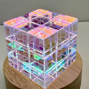 May include: An iridescent cube with a geometric pattern, set on a circular wooden base. The cube reflects colours like pink, purple, and green. The decorative cube is a unique item.