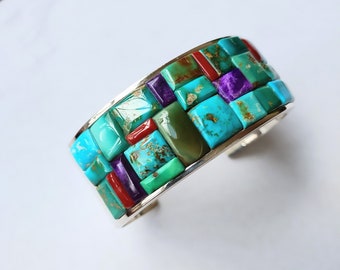 May include: A silver cuff bracelet with a mosaic of turquoise, green, purple, and red stones.