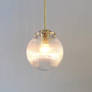May include: A brass pendant light with a clear, ribbed glass shade. The light is turned on and illuminating the room.