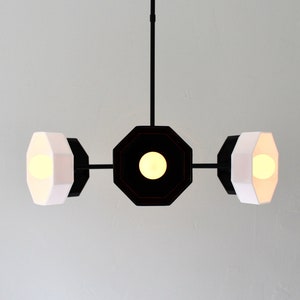 May include: A black and white pendant light fixture with three octagonal shades. The shades are white on the outside and black on the inside. The fixture has a black metal frame.