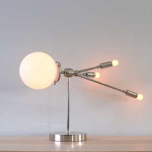 May include: A chrome table lamp with a white globe and three light bulbs. The lamp has a modern, geometric design.