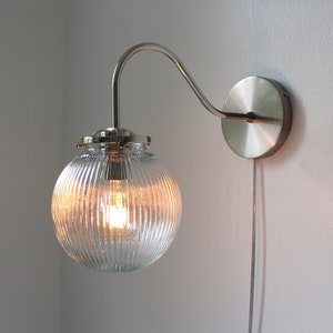 May include: A silver wall-mounted light fixture with a clear ribbed glass globe shade. The light is on and the bulb is visible.