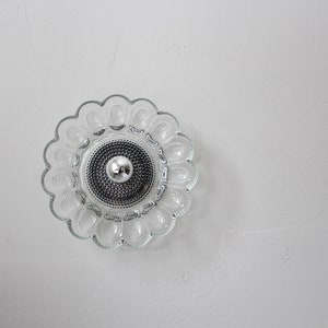May include: A clear glass ceiling light fixture with a flower-shaped design. The light fixture has a silver center with a small, round bulb.
