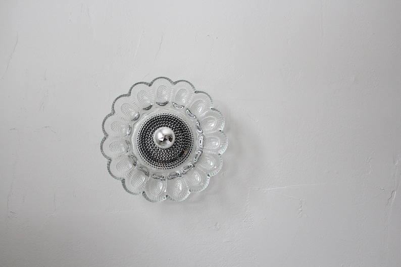 May include: A clear glass ceiling light fixture with a flower-shaped design. The light fixture has a silver center with a small, round bulb.