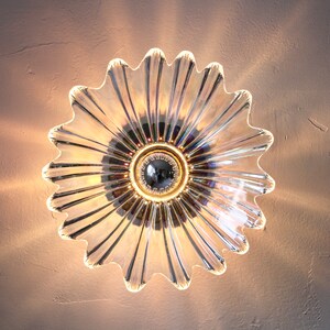 May include: A clear glass ceiling light fixture shaped like a flower with a chrome center. The light fixture is illuminated and casting a warm glow.