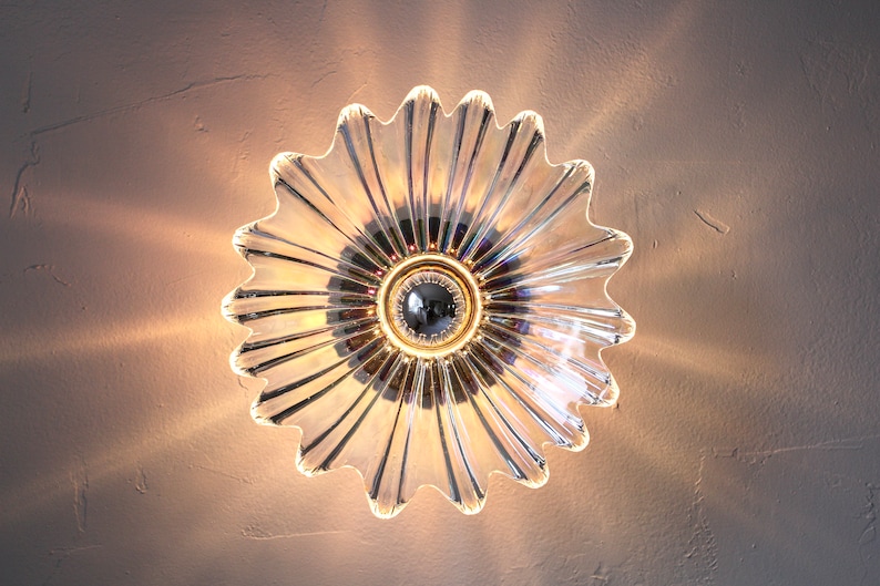 May include: A clear glass ceiling light fixture shaped like a flower with a chrome center. The light fixture is illuminated and casting a warm glow.