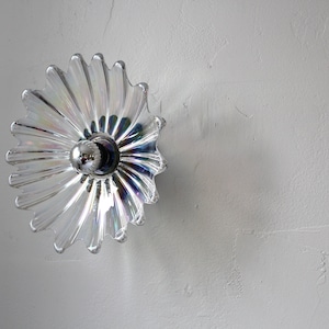 May include: A clear glass light fixture with a flower-shaped design. The fixture has a silver metal center with a single light bulb.