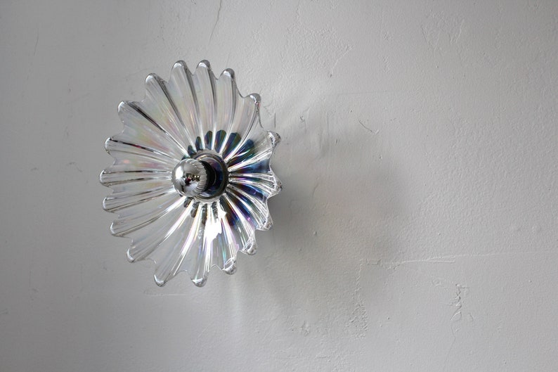 May include: A clear glass light fixture with a flower-shaped design. The fixture has a silver metal center with a single light bulb.