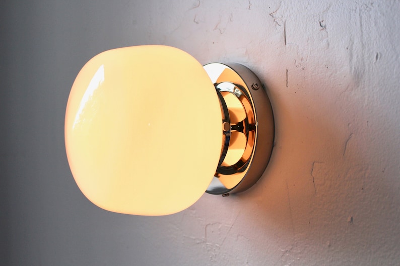 Op de afbeelding: Een chromen wandlamp met een matglazen bol. Het licht is aan en de bol gloeit.