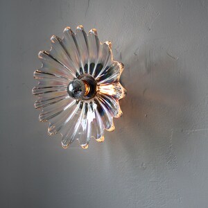 May include: A clear glass wall sconce with a iridescent finish and a silver metal base. The sconce has a flower-like shape with many petals.
