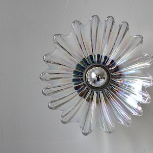 May include: A clear glass iridescent flower-shaped light fixture with a silver center and a light bulb.
