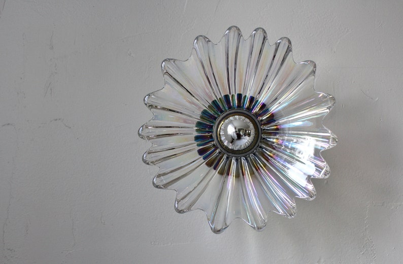 May include: A clear glass iridescent flower-shaped light fixture with a silver center and a light bulb.