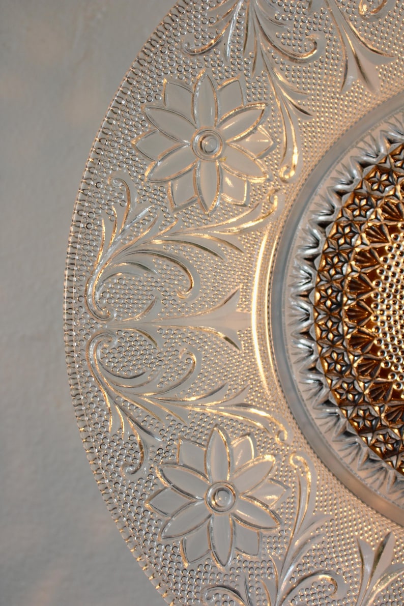 May include: Close-up of a clear glass plate with intricate floral and leaf patterns. The plate features embossed flowers and a textured background, with a detailed center design. The plate is a decorative piece.