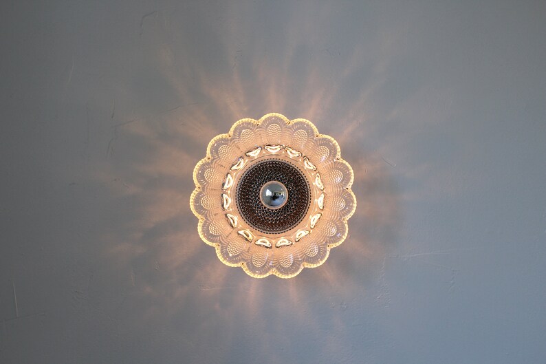 May include: A clear glass ceiling light fixture with a flower-shaped design. The light is on and casting a warm glow.