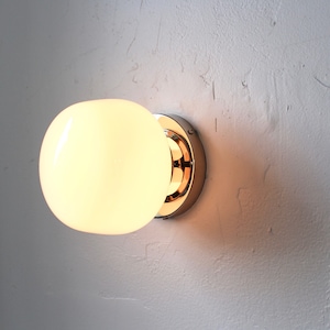 Op de afbeelding: Een chromen wandlamp met een witte, matte glazen bol. Het licht is aan en de bol is verlicht.