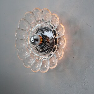 May include: A clear glass ceiling light fixture with a scalloped edge and a single light bulb in the center.