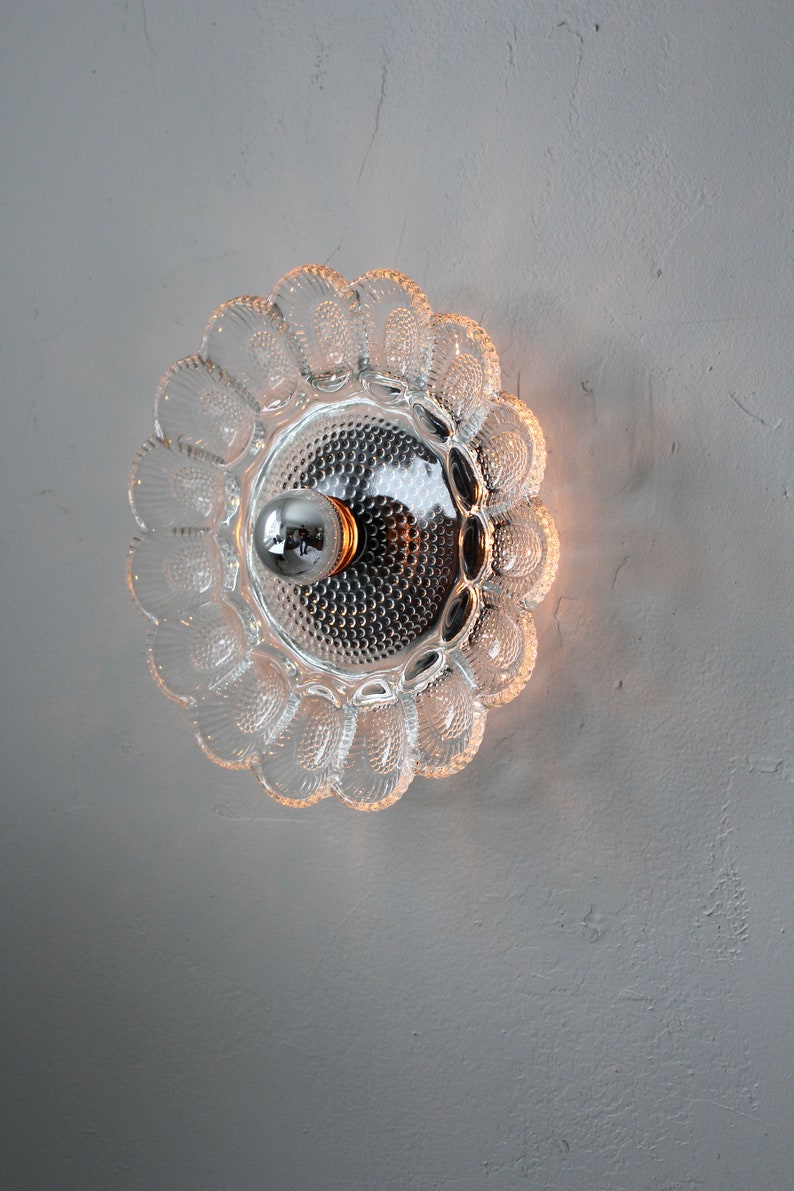 May include: A clear glass ceiling light fixture with a scalloped edge and a single light bulb in the center.