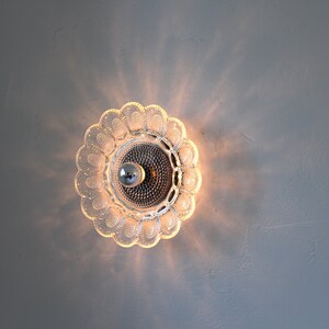 May include: A clear glass ceiling light fixture with a flower-shaped design. The light is on and casting a warm glow.