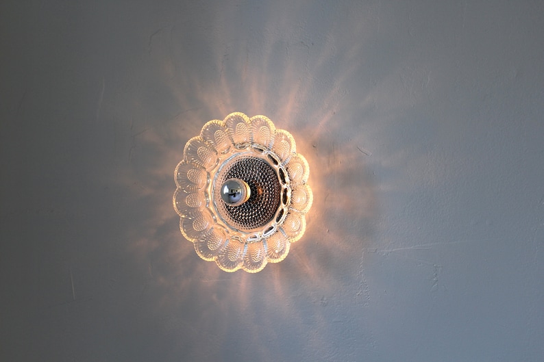 May include: A clear glass ceiling light fixture with a flower-shaped design. The light is on and casting a warm glow.