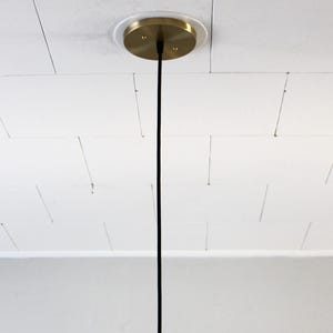 May include: A ceiling-mounted light fixture with a brass-colored canopy. A black cord descends from the canopy. The ceiling is white with a grid pattern.