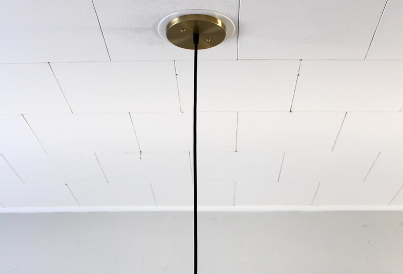 May include: A ceiling-mounted light fixture with a brass-colored canopy. A black cord descends from the canopy. The ceiling is white with a grid pattern.
