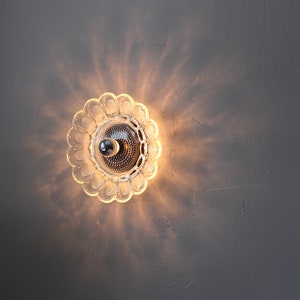May include: A clear glass ceiling light fixture with a decorative, scalloped edge. The light is on and casting a warm glow.