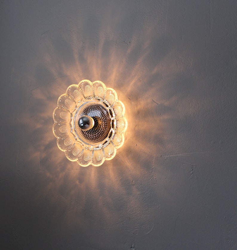 May include: A clear glass ceiling light fixture with a decorative, scalloped edge. The light is on and casting a warm glow.