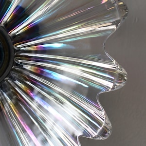 May include: Close-up of a clear glass lampshade with iridescent rainbow stripes. The lampshade has a scalloped edge and a round opening at the top.