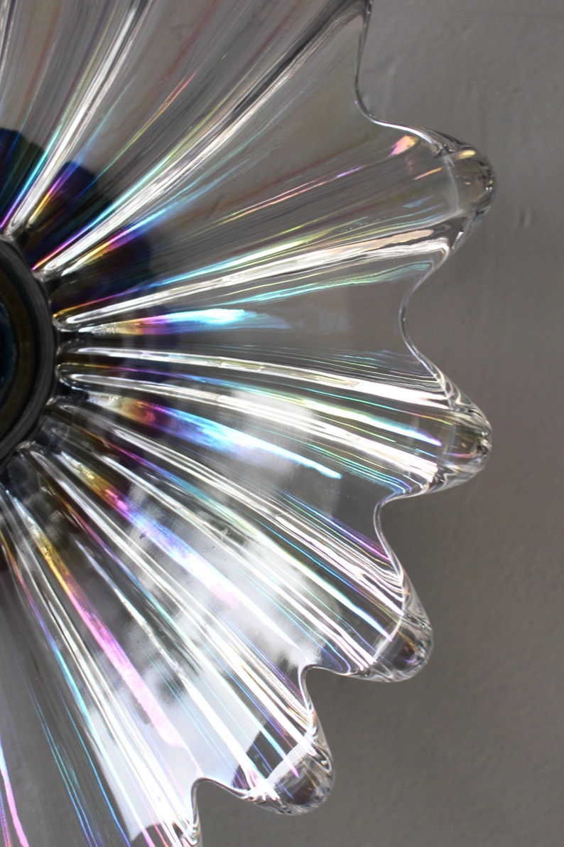 May include: Close-up of a clear glass lampshade with iridescent rainbow stripes. The lampshade has a scalloped edge and a round opening at the top.