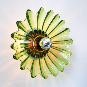 Puede incluir: Una lámpara de pared de vidrio verde con un diseño acanalado, que se asemeja a una flor. La lámpara tiene una toma de bombilla de plata y una base de color dorado.