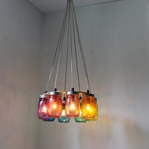 May include: A colorful chandelier made from glass jars with light bulbs inside. The jars are suspended from the ceiling by cords and are arranged in a circle.