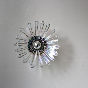 May include: A clear glass ceiling light fixture shaped like a flower with a silver bulb in the center.