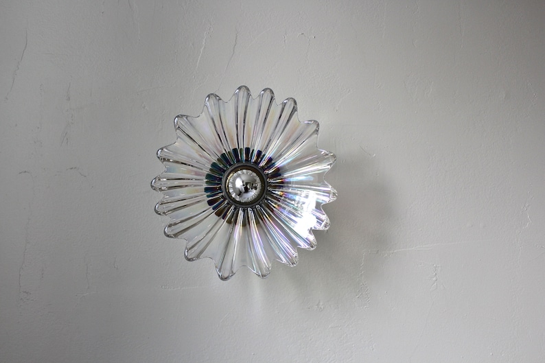 May include: A clear glass ceiling light fixture shaped like a flower with a silver bulb in the center.