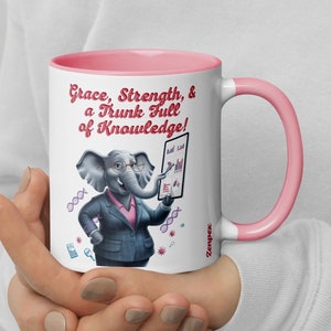 Puede incluir: Taza de cerámica blanca con borde y asa de color rosa. La taza presenta un elefante de dibujos animados con gafas y traje, sosteniendo un portapapeles con gráficos y tablas. El texto en la taza dice "Grace, Strength, & a Trunk Full of Knowledge!"