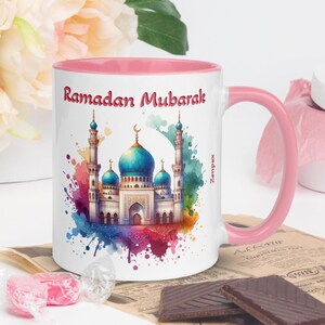 Peut inclure: Une tasse en céramique rose et blanche avec une illustration aquarelle d'une mosquée et le texte "Ramadan Mubarak".