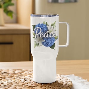 Op de afbeelding: Witte reistumbler van roestvrij staal met een blauw en wit bloemenmotief en het woord "Peace" in wit schrift.