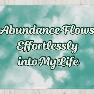 May include: A teal and white tie-dye throw blanket with the text "Abundance Flows Effortlessly into My Life" printed in white.