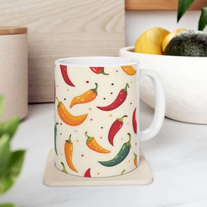Può includere: Tazza in ceramica bianca con un motivo colorato di peperoncini rossi, arancioni e verdi su uno sfondo crema.