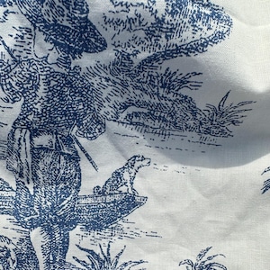 May include: White fabric with a blue toile pattern. The design depicts a pastoral scene with figures, trees, and a dog. The fabric has a detailed, vintage aesthetic.