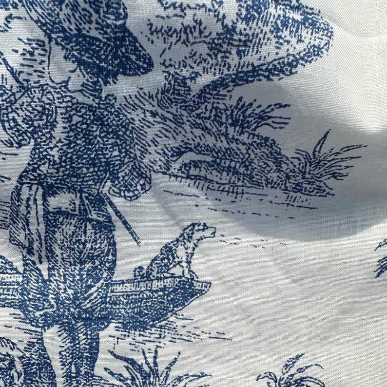 May include: White fabric with a blue toile pattern. The design depicts a pastoral scene with figures, trees, and a dog. The fabric has a detailed, vintage aesthetic.