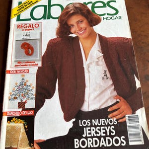 May include: A November 1989 issue of Labores del Hogar magazine featuring a cover with a person wearing a brown knit cardigan over a white collared shirt. The cover includes text such as Labores, Regalo, Ideas Navidad, Ganchillo de Lujo, and Los Nuevos Jerseys Bordados.