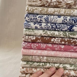 May include: A pile of fabric swatches in assorted colours and patterns. The fabrics display floral, toile, and botanical designs in shades of brown, blue, pink, and green. The swatches are neatly folded and stacked.