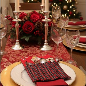 Puede incluir: Una mesa festiva con un esquema de color rojo y dorado. La mesa está decorada con platos con borde dorado, servilletas rojas y cubiertos en un soporte a cuadros. Copas de vino de cristal y candelabros plateados con velas encendidas completan la decoración navideña.