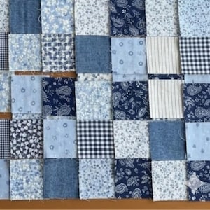 Könnte beinhalten: Ein Patchwork-Quilt in Blautönen, bestehend aus Quadraten aus Jeans-, Blumen-, Paisley- und Vichy-Stoffen. Die Anordnung erzeugt eine strukturierte, handwerkliche Ästhetik, ideal für Heimdekoration oder Bastelprojekte.
