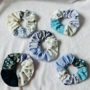 Könnte beinhalten: Fünf handgefertigte Haargummis in verschiedenen Blau-, Weiß- und Blumenmustern. Jedes Haargummi hat ein einzigartiges Patchwork-Design mit einer Mischung aus Streifen, Karos und unifarbenen Stoffen. Diese Haaraccessoires sind perfekt, um einen Hauch von Stil zu verleihen.