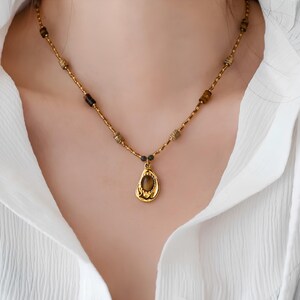 May include: A gold necklace with a teardrop-shaped pendant featuring a brown gemstone. The necklace is made of small gold beads and a chain.